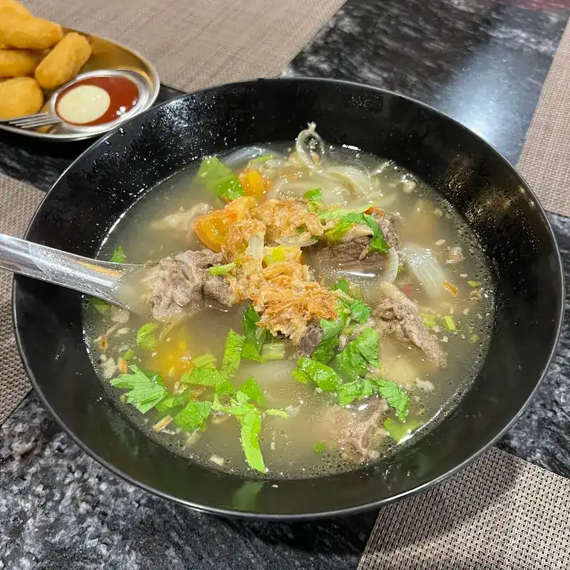 Beef soup in a black bowl, with coriander and fried shallots