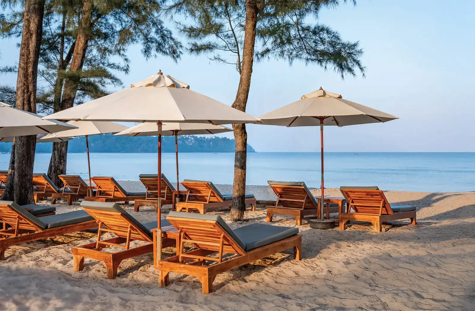 Teak sunbeds under white umbrellas on the sand, with the sea behind