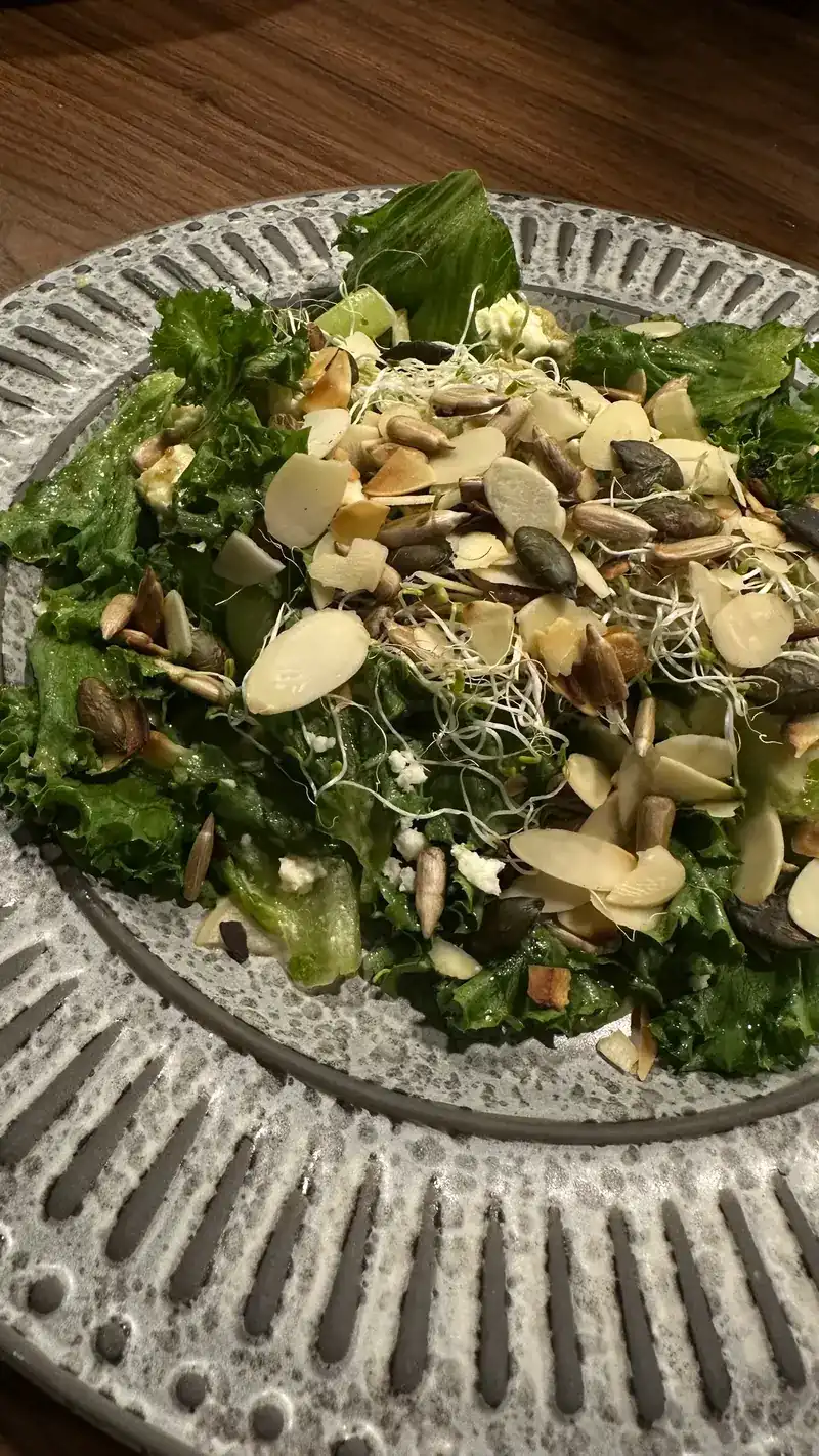 A green salad topped with almond flakes, pumpkin seeds and sprouts