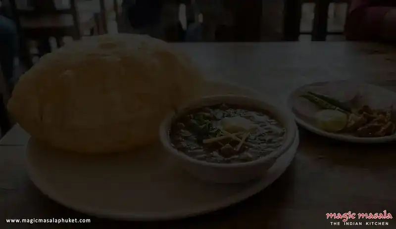 A puffed fried bread beside a bowl of chickpea curry