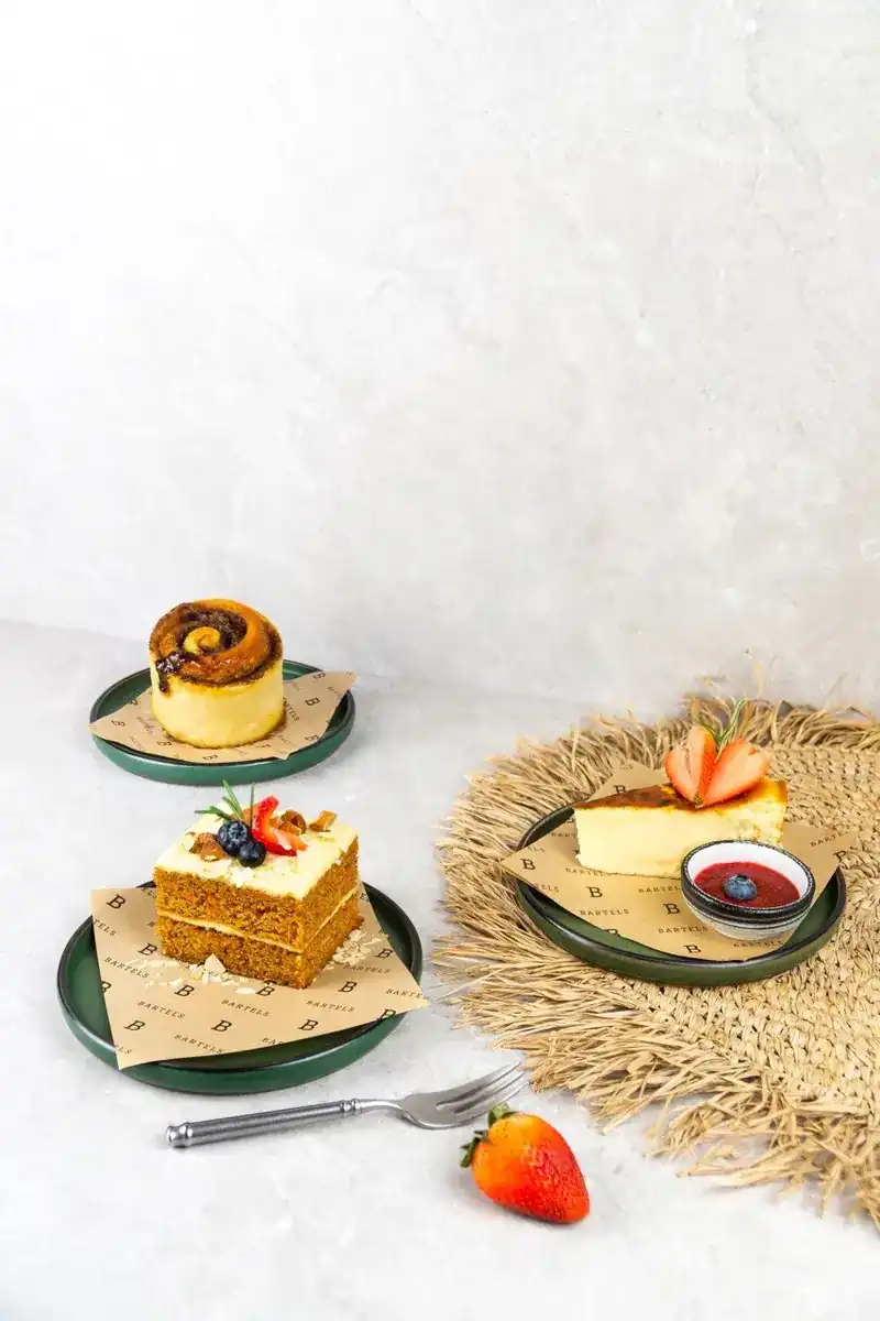 A cinnamon roll, carrot cake and cheesecake with strawberry on green plates