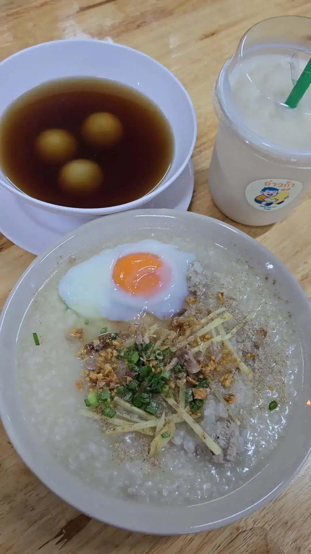 Rice soup with pork and a soft egg, black sesame balls in ginger syrup, and an iced soy milk in a Taoka cup