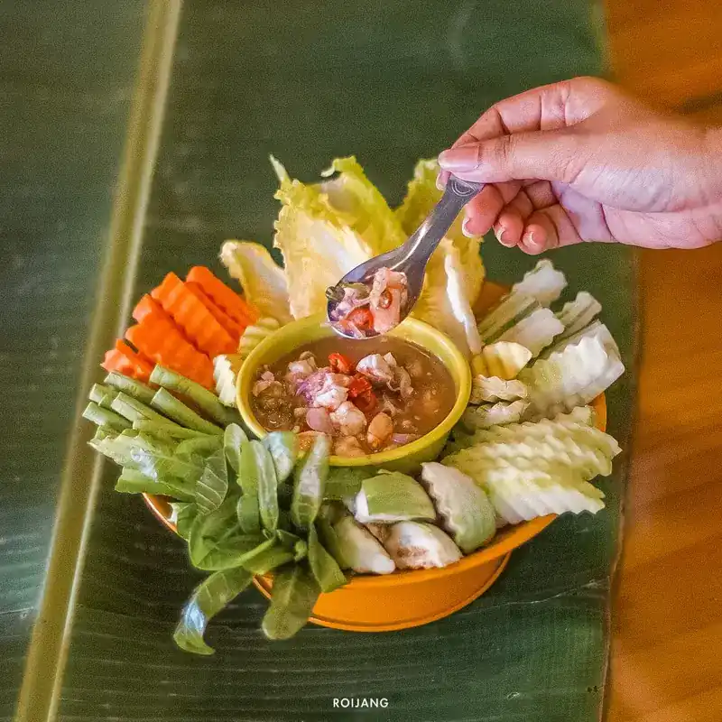 A bowl of chili dip ringed with fresh vegetables, a spoon lifting some