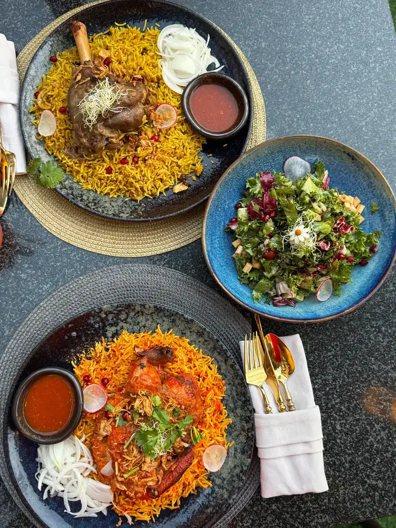 Seen from above: a lamb shank on yellow rice with a red sauce, a green salad in a blue bowl, and chicken on orange spiced rice