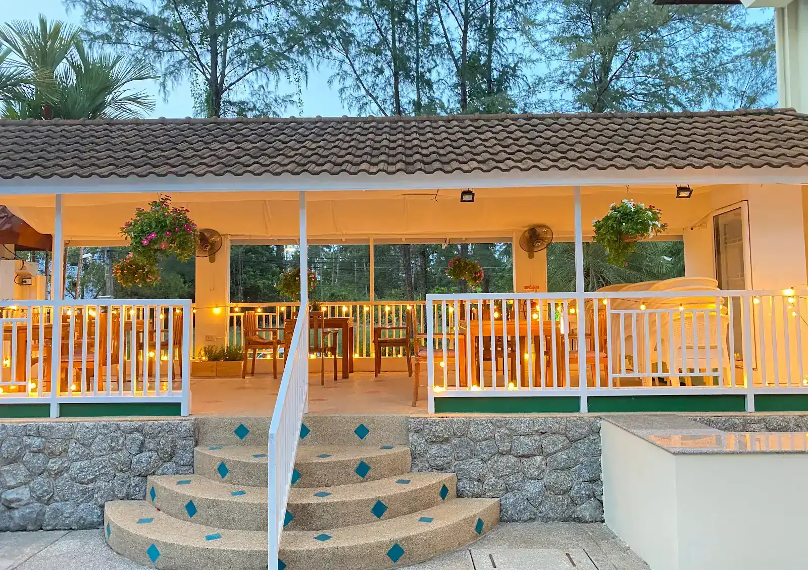 The covered veranda at Da Babbo at dusk, small lights along the white railing and tiled steps leading up