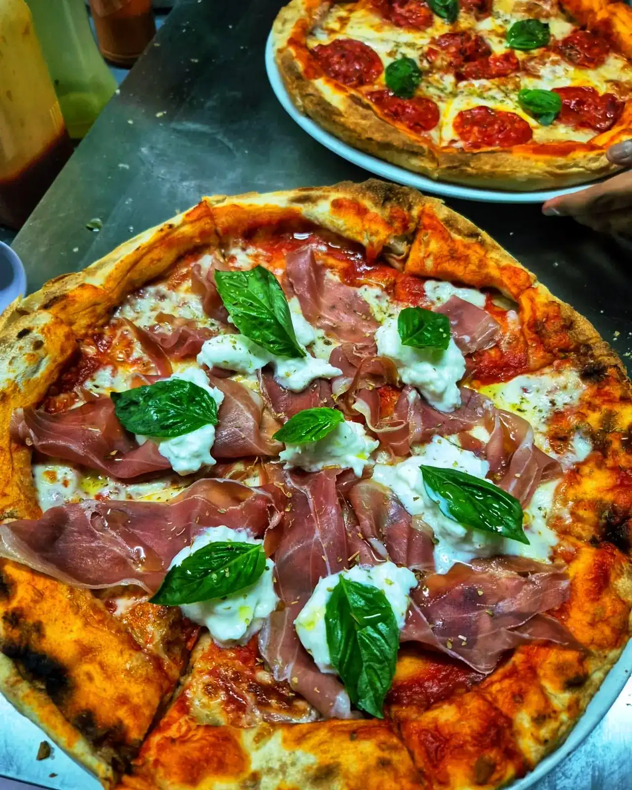 Pizza with raw ham, burrata and fresh basil, a second pizza behind it