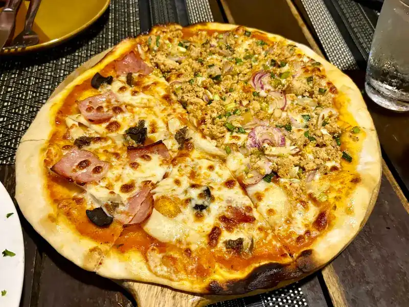 A thin-crust pizza with two toppings: ham on one half, minced meat with red onion and herbs on the other