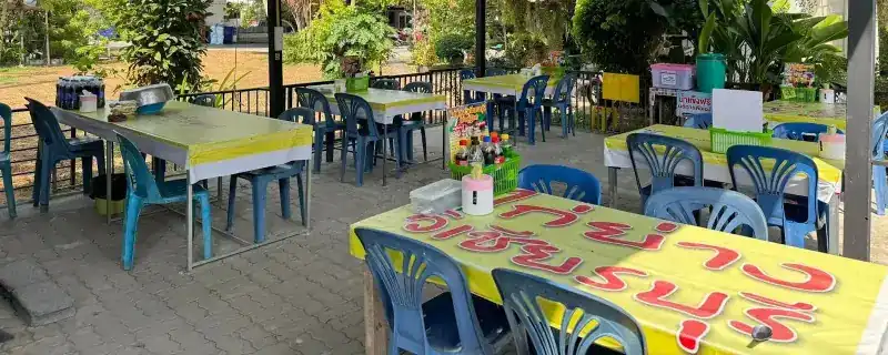 The seating: tables with yellow covers and blue chairs under a tin roof, the shop's name painted on the nearest tablecloth