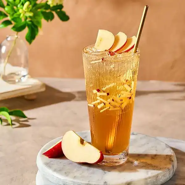 A tall glass of amber cold brew tea with slices of fresh apple