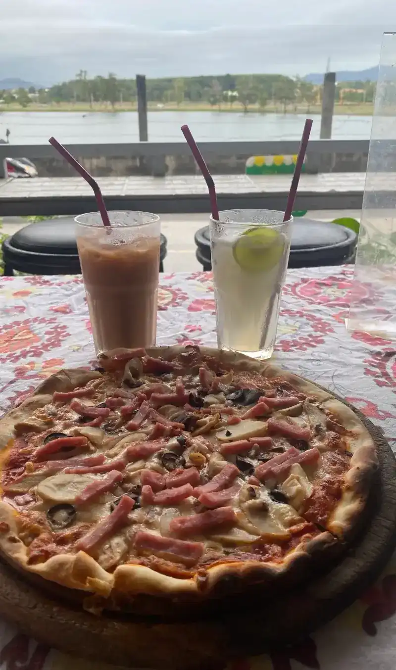 Pizza and two iced drinks on a table, with water and hills behind