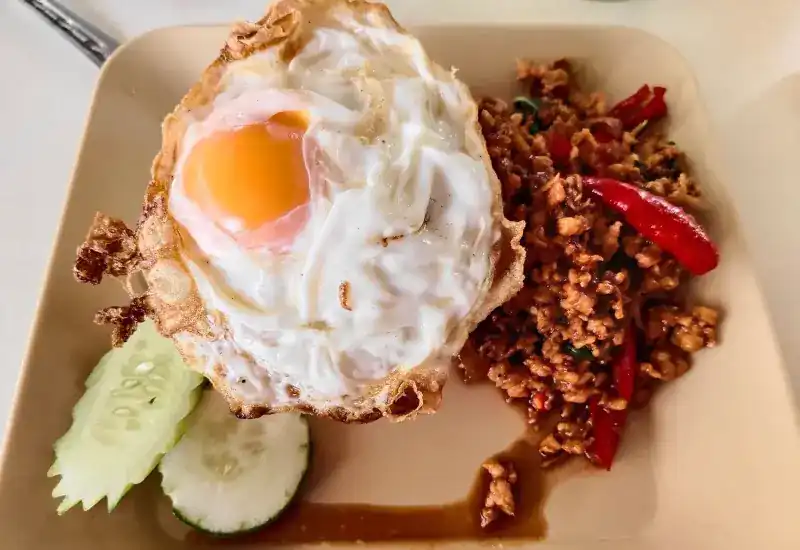 A chilli stir-fry topped with a crisp fried egg, cucumber on the side
