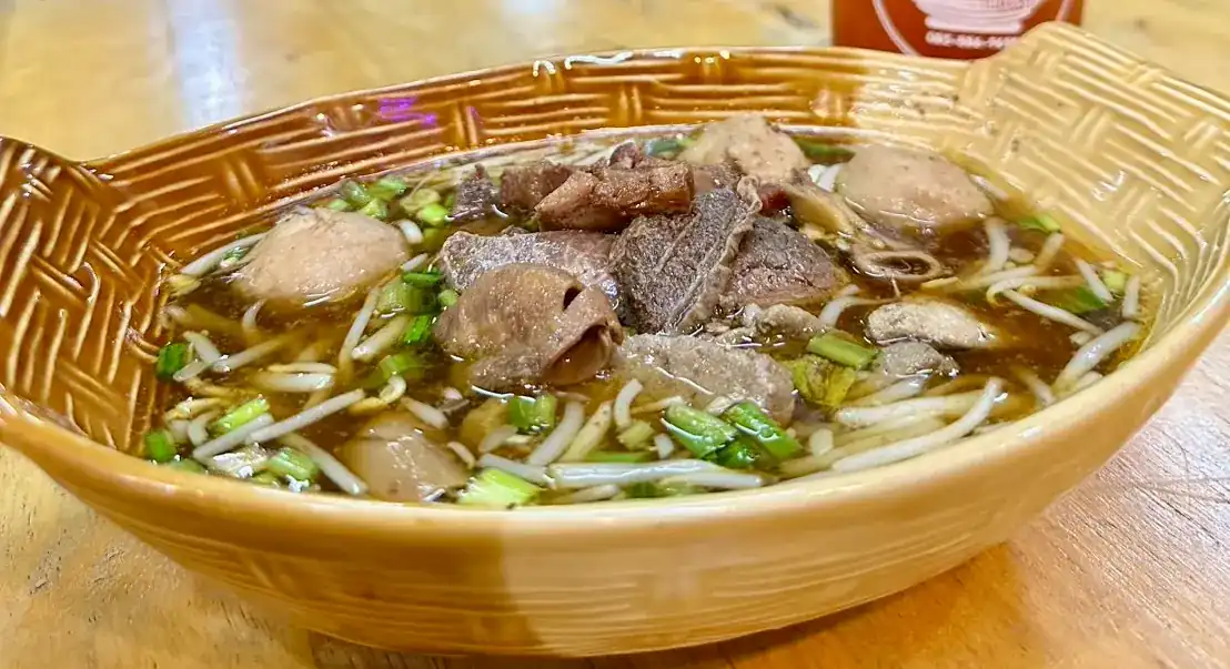 Boat noodles with sliced beef, meatballs, bean sprouts and spring onion in a basket-weave ceramic bowl