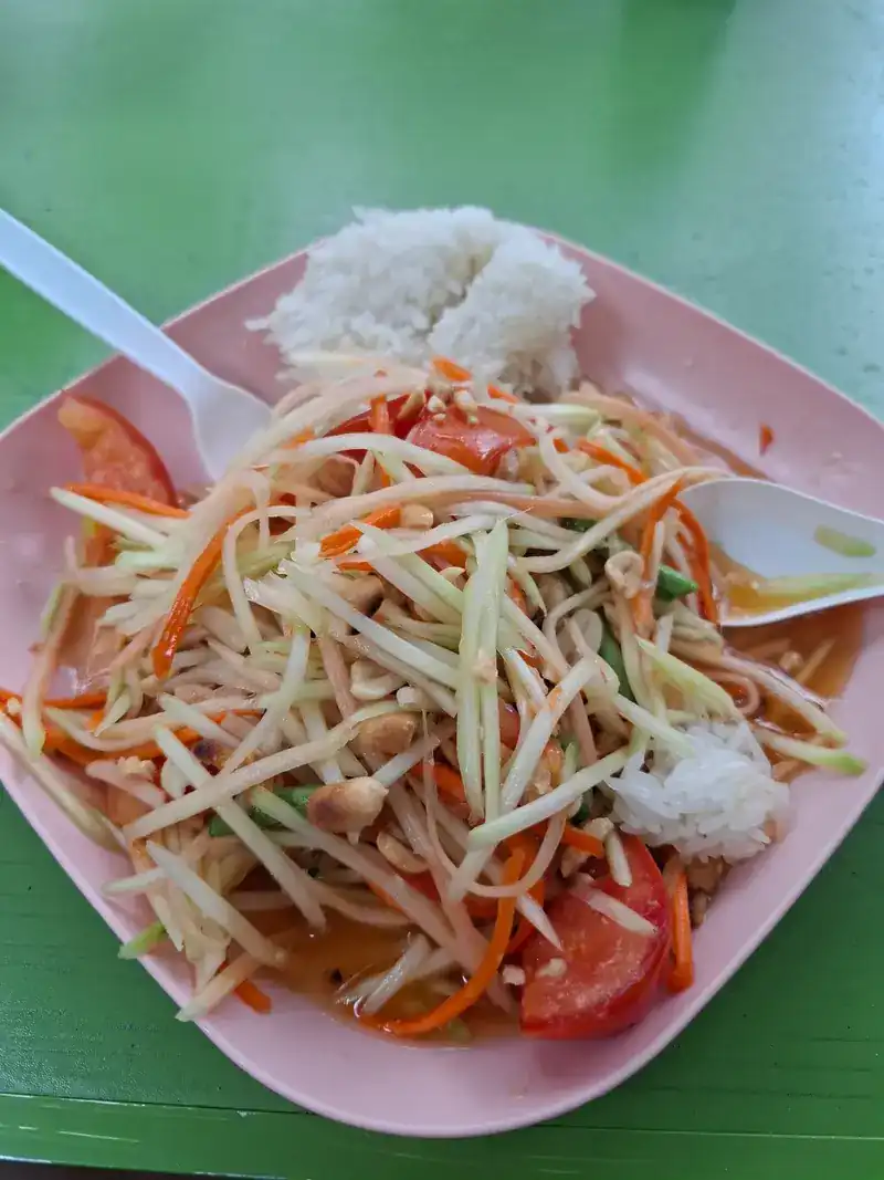 Papaya salad with tomatoes and peanuts, with rice, on a pink plate