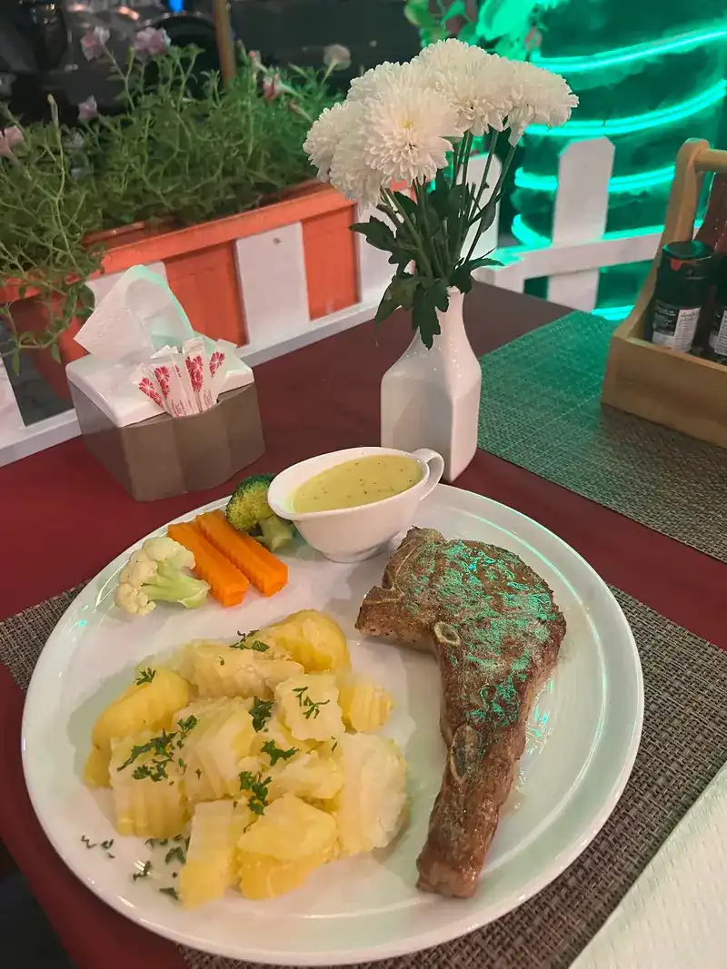Steak with potatoes, vegetables and a jug of sauce on the terrace at night