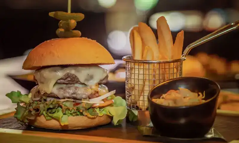 Cheeseburger topped with pickles, fries in a wire basket and coleslaw