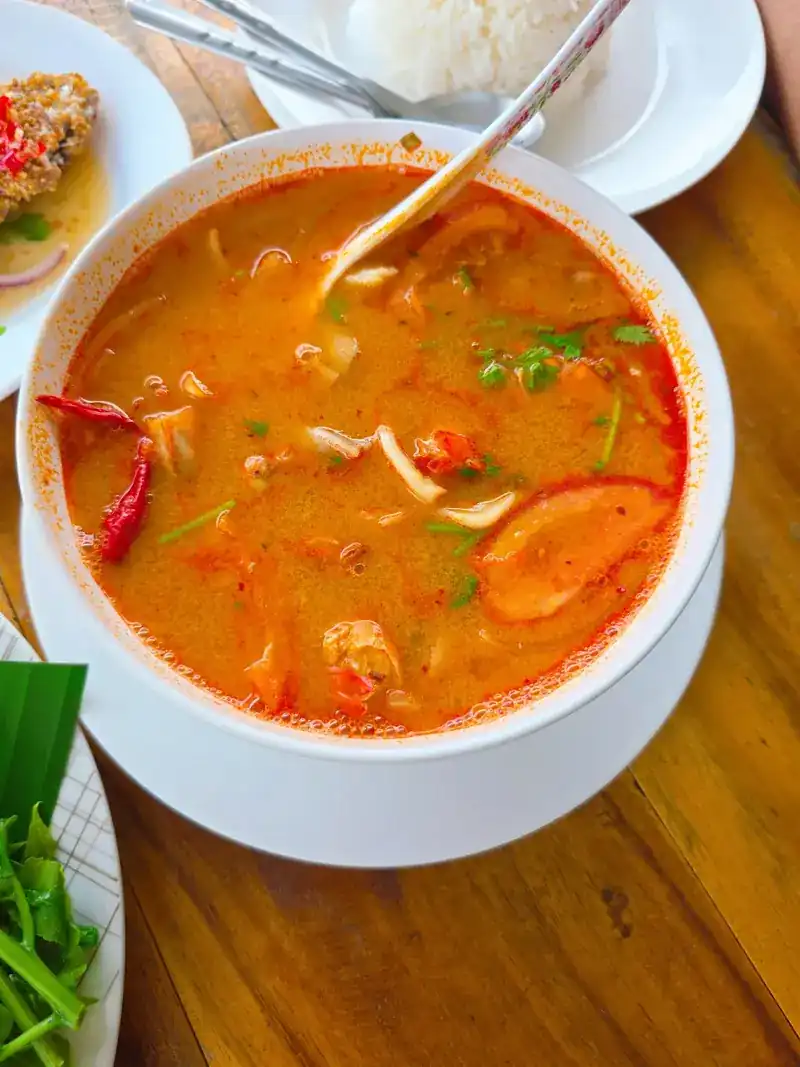 A bowl of red-orange broth with dried chillies, rice on the side