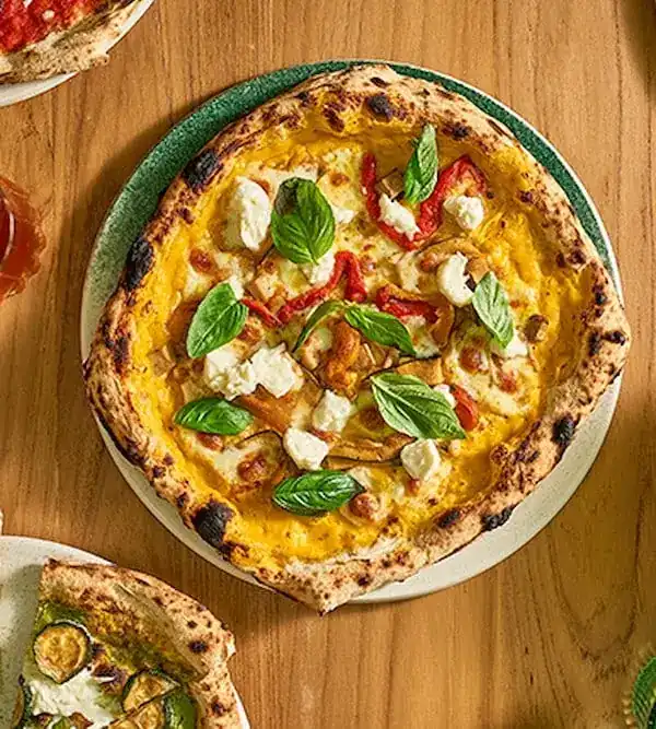 A wood-fired pizza with basil and mozzarella on a green plate