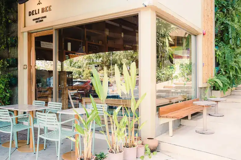 The corner shopfront at Blue Tree Phuket: mint-green chairs, a teak bench and the DELI BEE sign