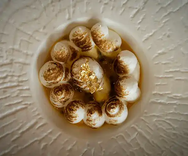 A dessert of torched meringue drops with gold leaf, seen from above