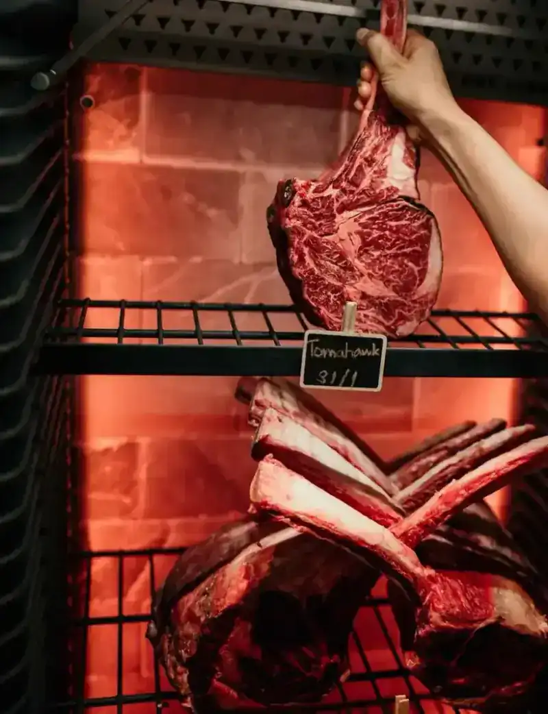 A hand lifting a marbled tomahawk from the dry-ageing cabinet