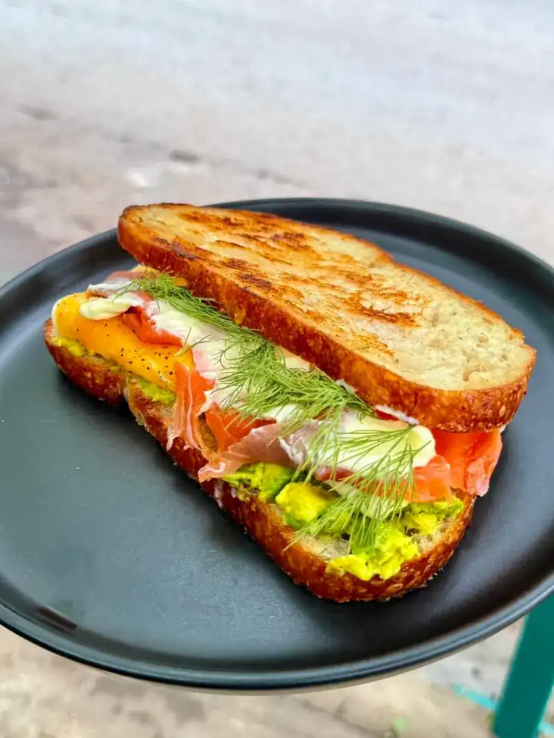 A toasted sourdough sandwich with salmon, avocado and dill