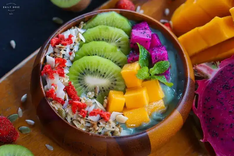 Smoothie bowl in a wooden bowl topped with kiwi, mango, dragon fruit and granola / สมูทตี้โบวล์ในชามไม้ ท็อปกีวี มะม่วง แก้วมังกร และกราโนล่า