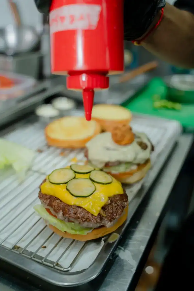 Burgers being built in the kitchen: cheddar, pickles and a squeeze of sauce / ประกอบเบอร์เกอร์ในครัว ชีสเชดดาร์ ผักดอง และซอส