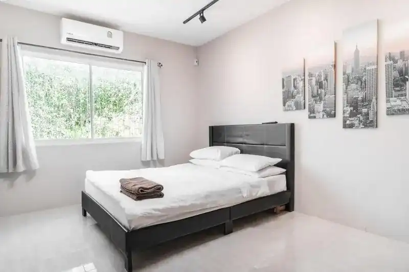 A Breakers hotel room: double bed, white walls, window onto greenery and air conditioning