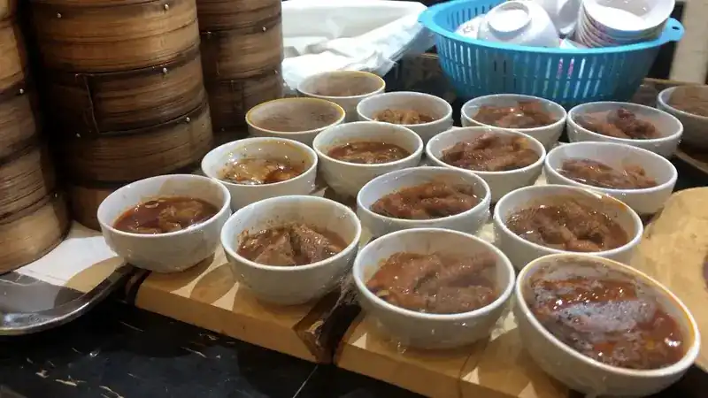 Bowls of braised dishes in a dark broth, lined up beside the stacked steamers