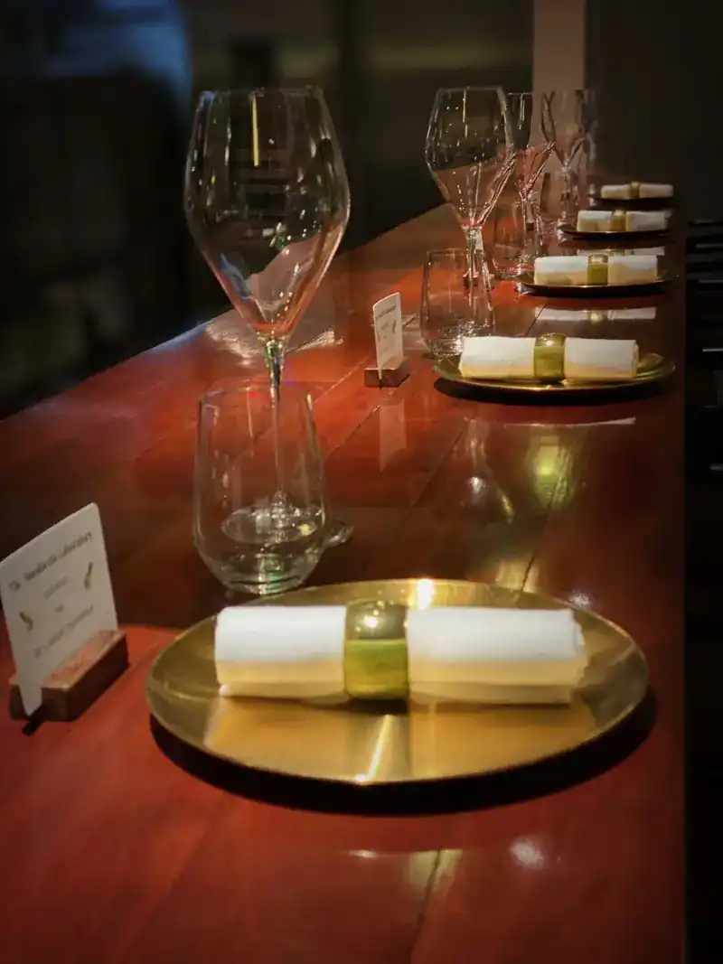 Places set along the polished wooden kitchen counter, with brass plates and rolled napkins