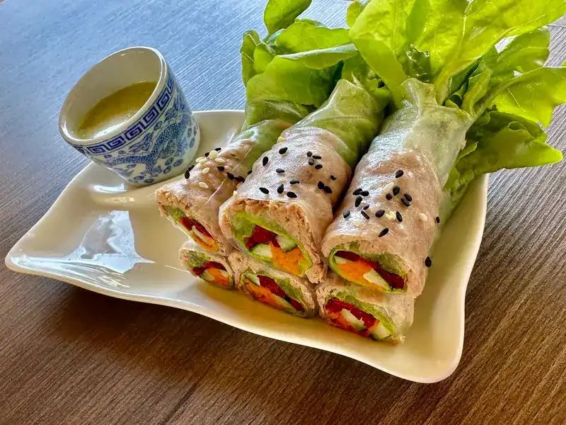Fresh vegetable rolls sprinkled with black sesame, with lettuce leaves and a cup of dipping sauce