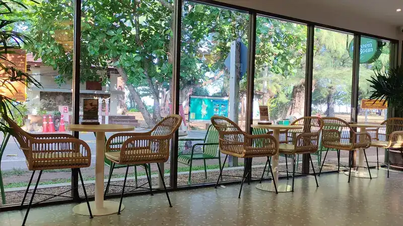 Rattan chairs and round tables along the café's tall windows, with trees outside