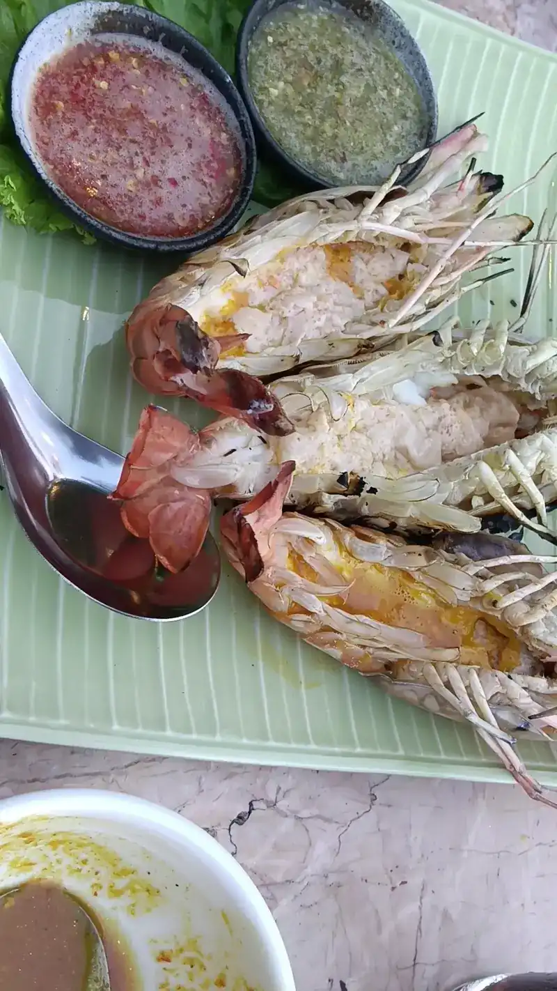 Grilled prawns split in half on a banana leaf, with two dipping sauces