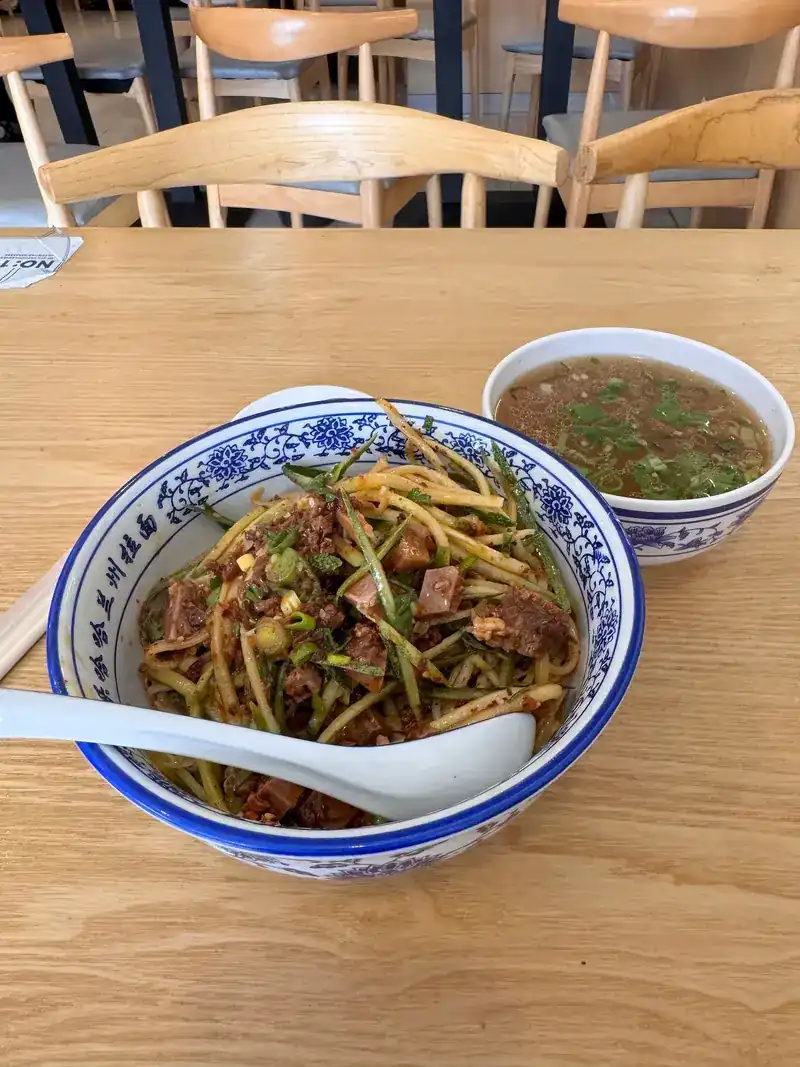 Dry noodles tossed with beef and vegetables, a small bowl of soup on the side