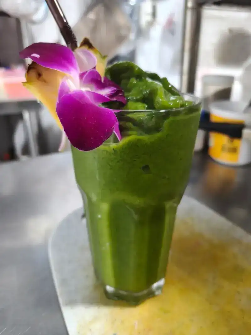 A green smoothie garnished with an orchid and pineapple