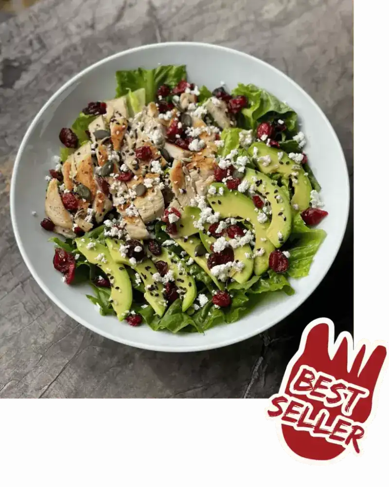 A salad of grilled chicken, avocado, dried berries and crumbled cheese