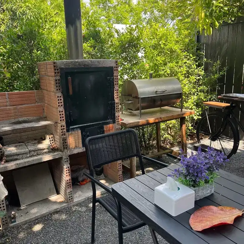 A brick smoker with a black steel door and a steel barrel grill in the garden, beside a table
