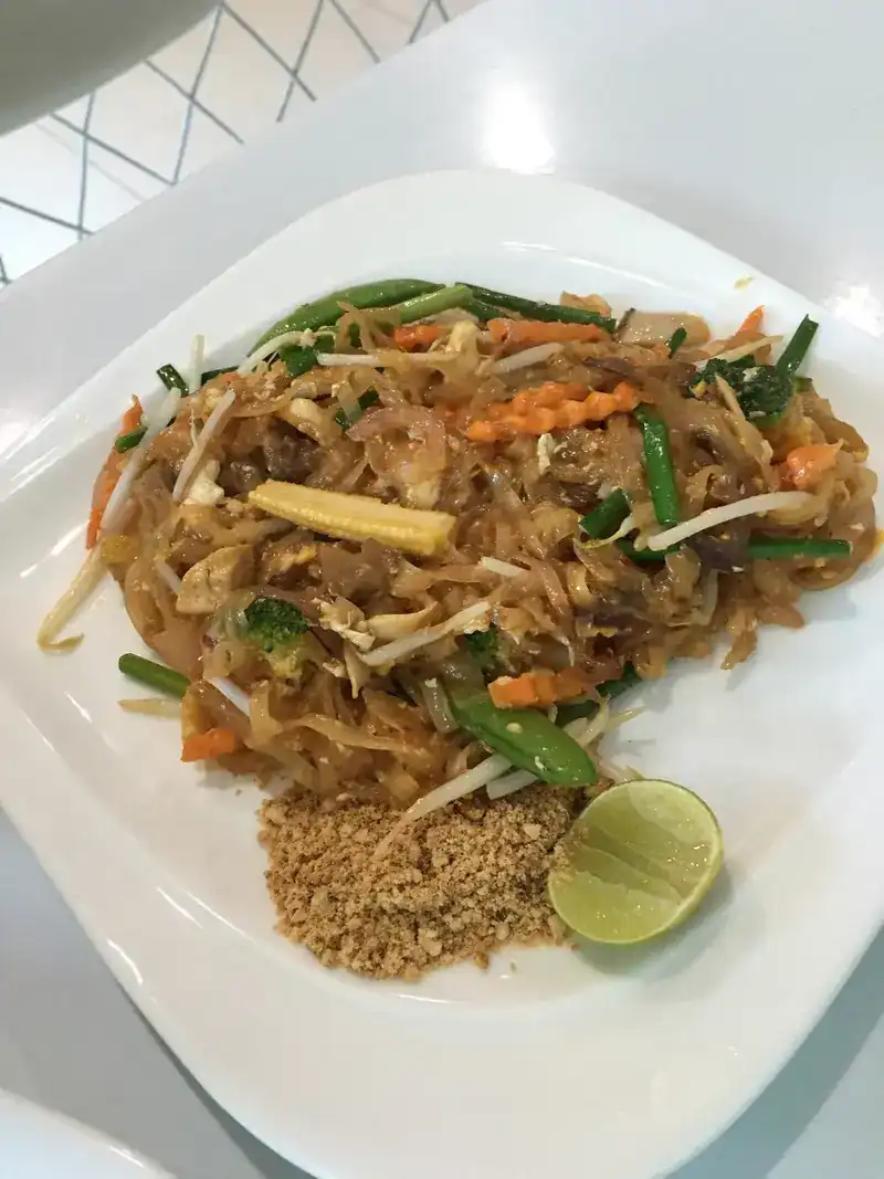 Stir-fried rice noodles with vegetables, crushed peanuts and half a lime on a white plate