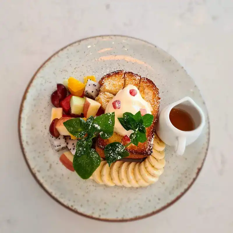 Thick toast with fresh fruit, sliced banana and a jug of syrup