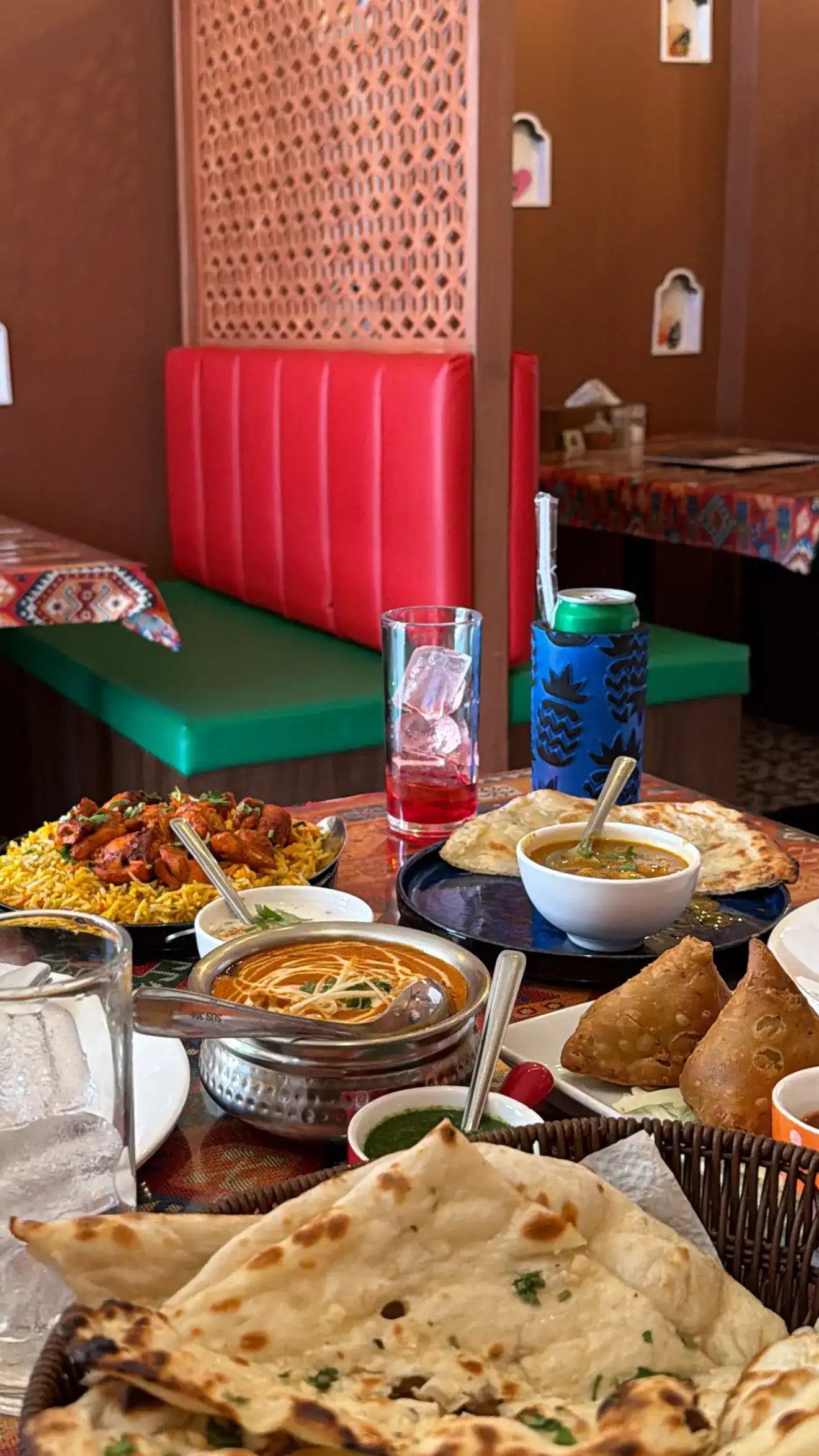 Biryani, a creamy curry, samosas and a basket of naan on a table by the red booth and the carved screen
