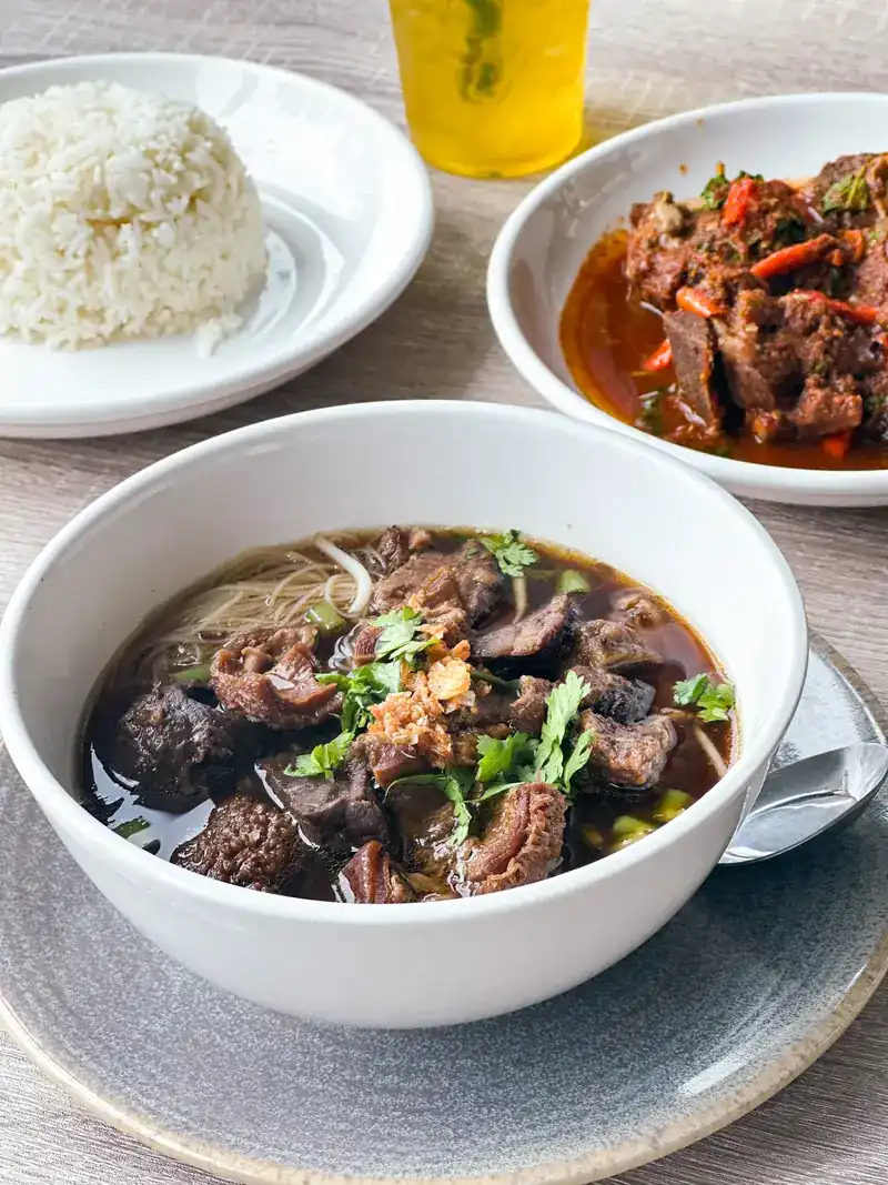 A bowl of beef noodle soup, braised beef in red sauce and a plate of rice