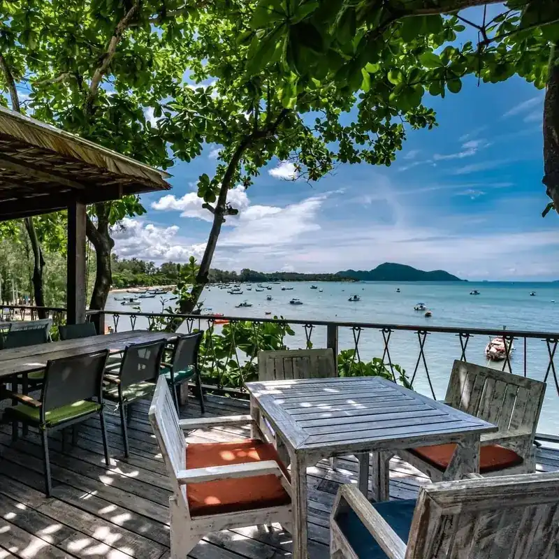 Tables on the deck under the trees, looking across the bay to the hills