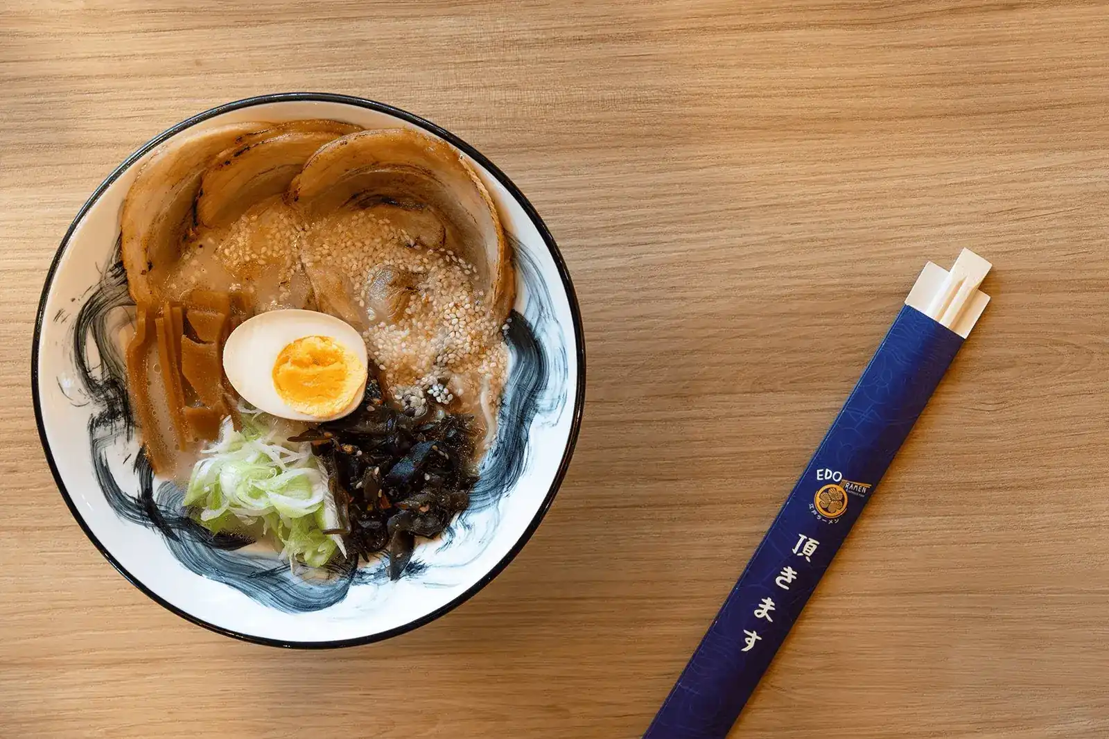 A bowl of ramen seen from above: rolled chashu, half a soft egg, spring onion and sesame