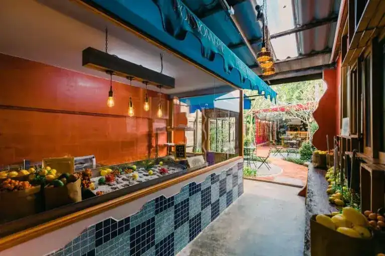 The covered market passage: a fish counter on ice under a blue awning, crates of fruit, the garden beyond