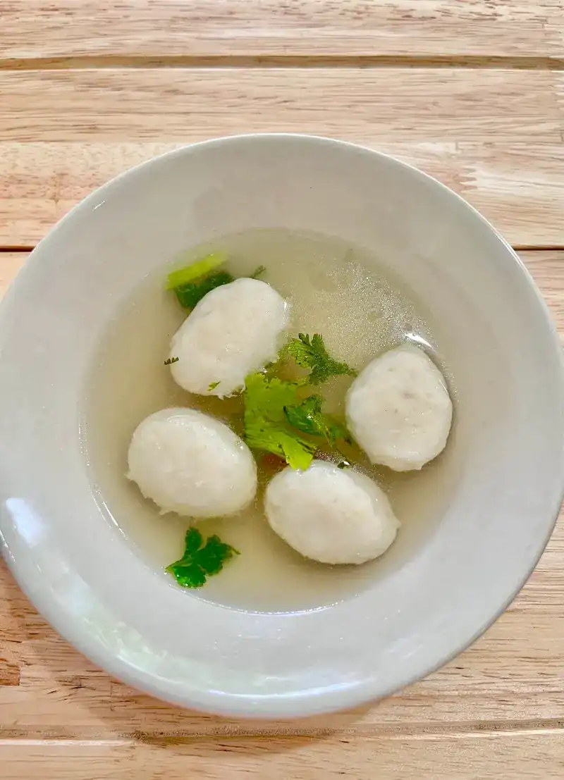 Fish balls in clear soup with coriander, on a wooden table