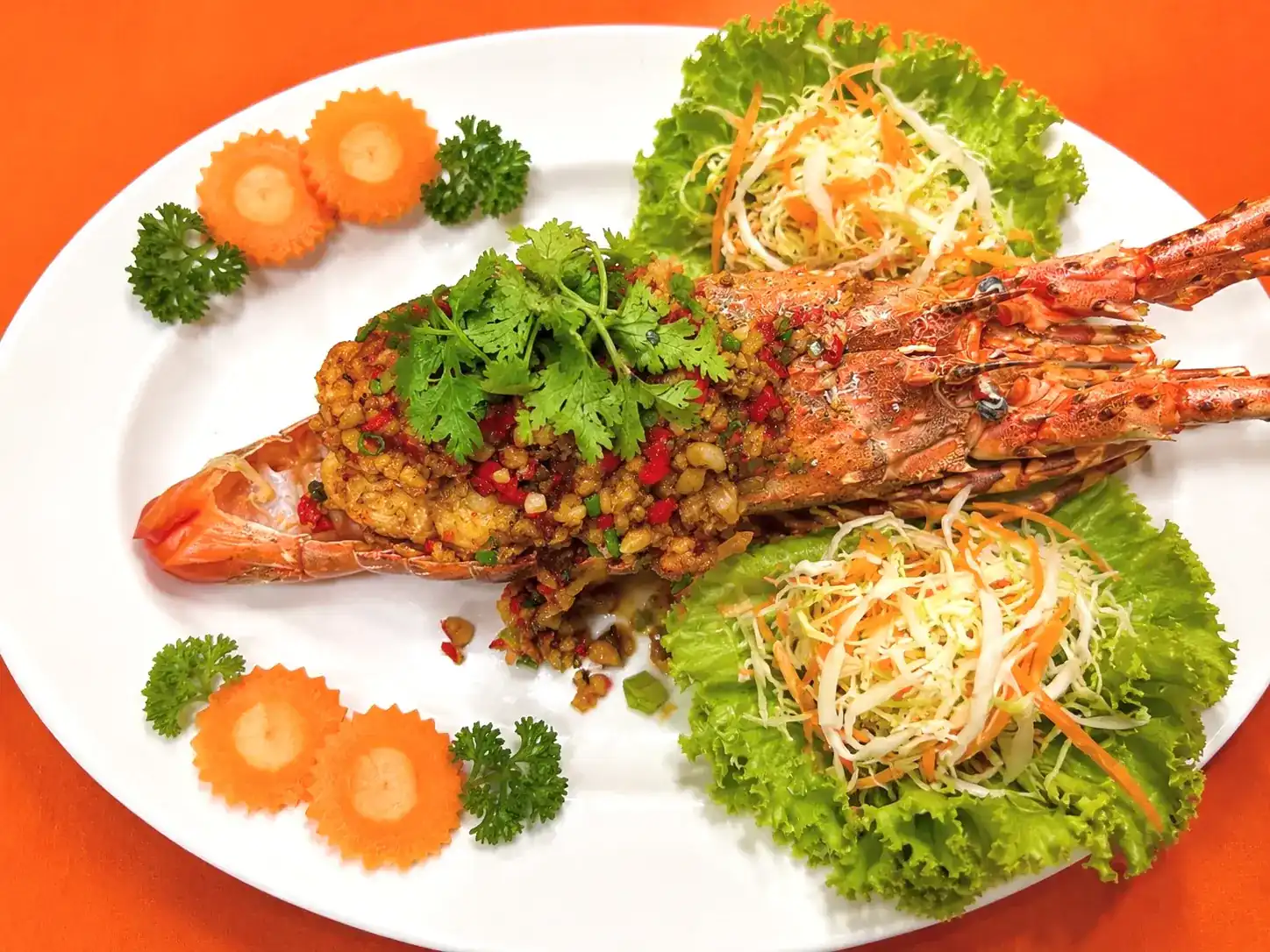 A whole lobster, split and topped with chilli and garlic, on a white plate