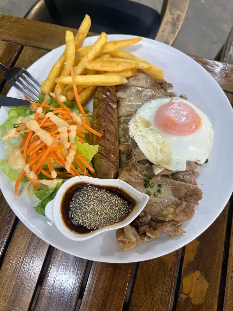 Steak plate with a fried egg, sausage, fries, salad and black pepper sauce