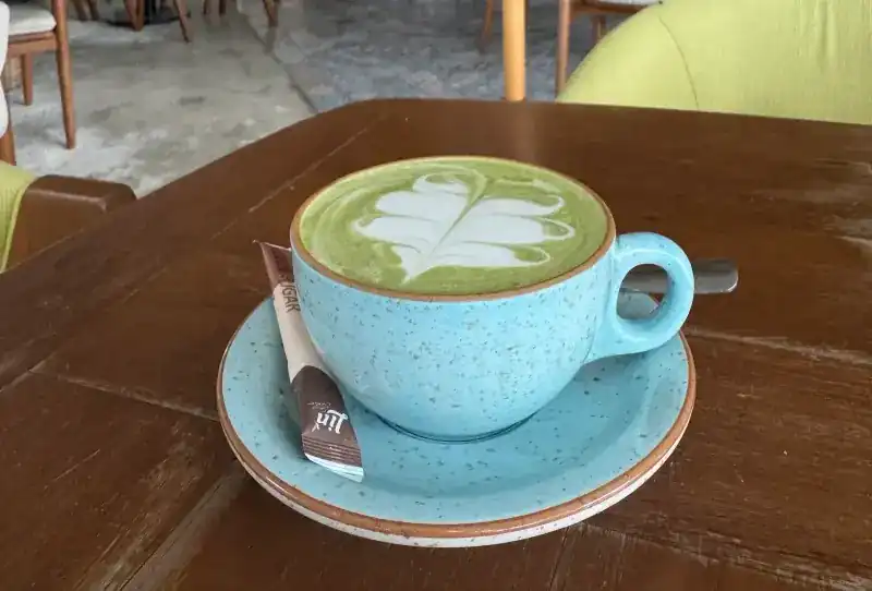 Matcha latte with leaf art in a speckled blue cup on a wooden table
