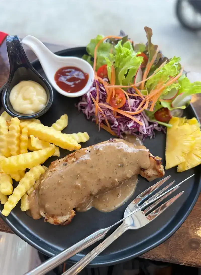 Steak under a brown sauce with crinkle-cut fries, salad, pineapple and two dips on a black plate