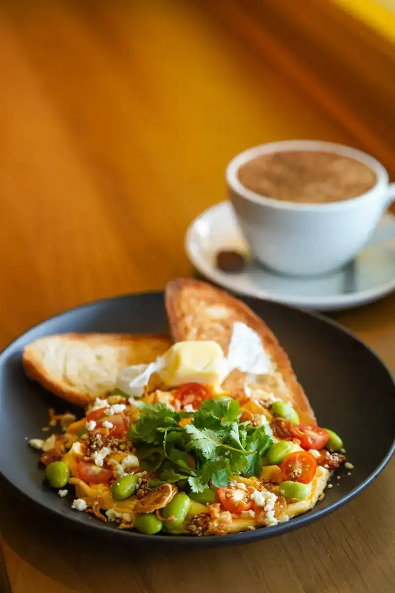 Eggs with herbs, tomatoes and toast, a hot coffee behind